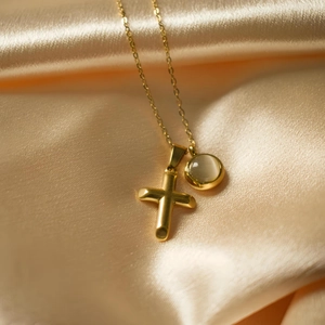Golden cross necklace with opal stone pendant displayed on elegant champagne silk fabric