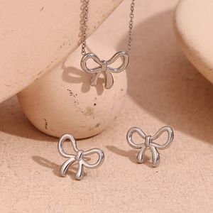 Macro shot of silver bow pendant necklace and stud earrings set on a textured stone