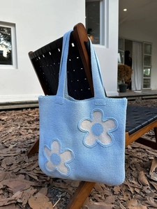 Detail of light blue knit tote bag with large floral appliques on a wooden chair
