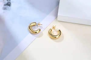 Macro shot of polished gold hollow C-shaped hoop earrings on a minimalist background
