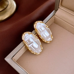 Close-up of vintage gold-rimmed oval pearl earrings with H-embossed detail in a jewelry box