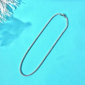 Detailed top view of sparkling silver tennis necklace with clear zircons on blue background