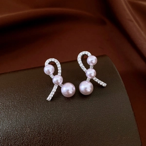Detailed macro view of silver bow earrings with three dangling pink pearls and zircons