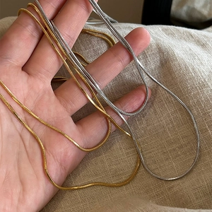 Detail of gold and silver snake chain necklaces showing metallic texture on linen