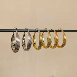 Détail de boucles d'oreilles créoles multicouches dorées et argentées sur un support noir