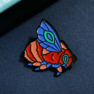 Macro shot of colorful enamel bee brooch with detailed red and blue wings on dark background