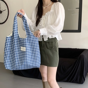 Close-up of blue and white checkered knit tote bag held by a model in casual setting