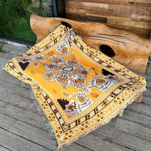 Detail of bohemian woven outdoor blanket featuring yellow floral patterns and fringe edges