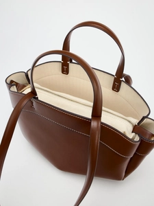 Brown leather tote bag with white stitching and beige canvas inner pouch on white background