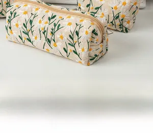 Detailed close-up of white daisy floral embroidery on a beige canvas cosmetic bag