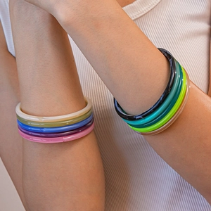 Colorful resin acrylic bangles in multiple shades worn by a model on white background