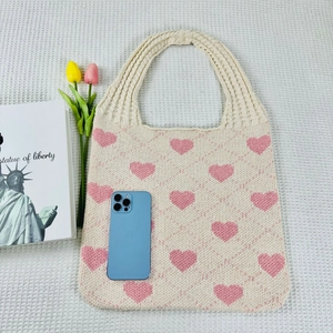 Knitted heart tote bag next to tulips and a phone showing its compact size