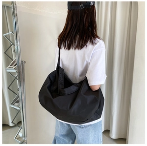 Detail of a black large-capacity nylon tote bag worn on shoulder showing texture and size