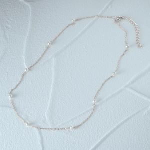 Detailed close-up of a delicate silver pearl necklace on a white textured background