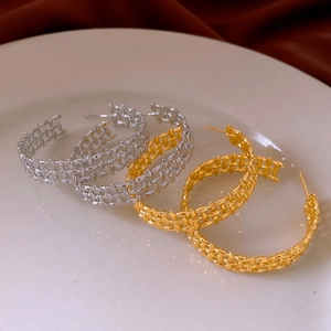 Close-up of gold and silver plated woven hollow C-shaped hoop earrings on white plate