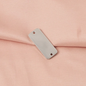Macro detail of polished stainless steel rectangular tag with dual holes on pink fabric