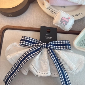 Detailed close-up of a white lace bow hair clip with a blue checkered ribbon on a tray