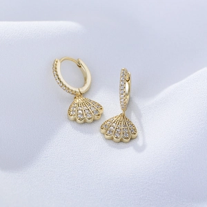 Macro shot of gold shell earrings with pavé white zircon stones on white fabric