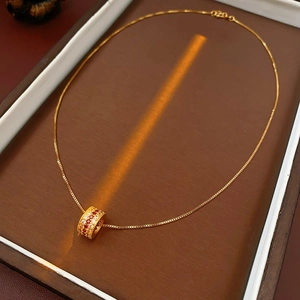Macro shot of gold cylinder pendant with red and white zircon stones on box chain necklace