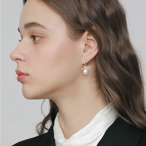 Close-up of golden bow earrings with pavé zircons and elegant white drop pearls on model
