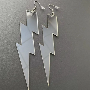 Detailed view of silver mirror acrylic lightning bolt earrings on a dark textured background