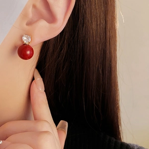 Détail d'une boucle d'oreille dorée avec pendentif boule rouge et zircon sur mannequin