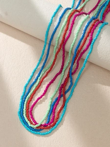 Detail of colorful Bohemian seed bead body chains draped on a beige cylinder pedestal