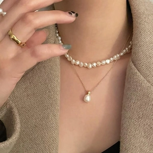 Minimalist double layered pearl necklace with gold ring on khaki wool blazer background