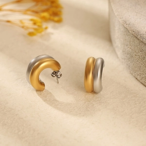 Détail de boucles d'oreilles en C bicolores avec finition mate brossée et texture or 18 carats