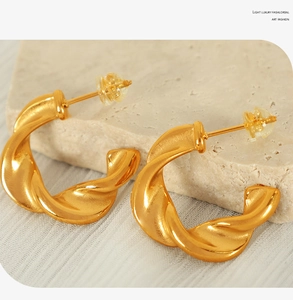 Detailed view of gold twisted C-shaped earrings on natural stone display base