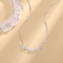 Detail of silver chain necklace featuring three delicate flower pendants on a warm beige backdrop