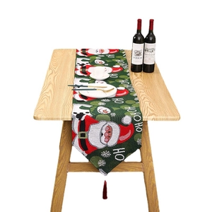 Christmas table runner with Santa Claus, snowmen and red tassels on a wooden dining table