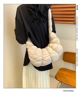 Rear view of a model wearing a puffy beige pleated crescent bag with quilted texture
