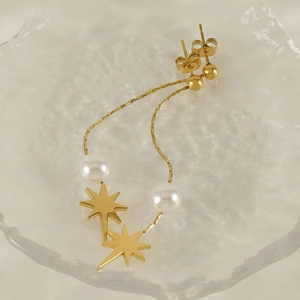 Elegant gold octagram star drop earrings with white pearls and tassels on glass surface