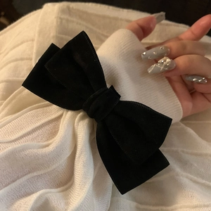 Elegant black velvet bow hair scrunchie shown on white knit sweater sleeve