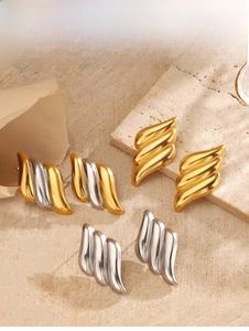 Détail des boucles d'oreilles texturées en finitions or et argent sur fond de pierre