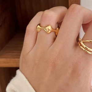 Close-up of minimalist gold geometric rings worn on model fingers with a warm wood background