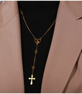 Detailed view of long gold cross necklace with hollow heart connector on a model