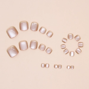 Detail of 24 champagne cat-eye fake toenails with gold glitter tips on a beige surface