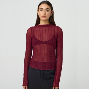 Close-up of semi-transparent burgundy knit top featuring a vertical pleated texture
