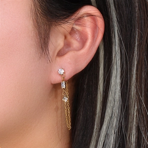 Detail of gold chain earrings with geometric white zircons worn on ear lobe