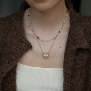 Detail of layered gold-plated necklaces featuring pearls and rhinestone pendant on model