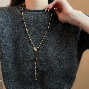 Detail of Y-shaped necklace with tiger eye beads and golden leaf charm on grey sweater