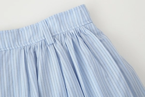 Close-up of light blue striped skirt waistline with belt loops and pleated fabric details