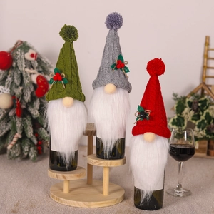 Three Christmas gnome wine bottle covers in green, grey, and red on a rustic wooden stand