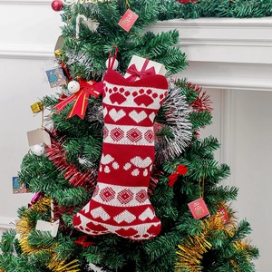 Knitted bone-shaped Christmas stocking with heart and paw patterns on a holiday tree