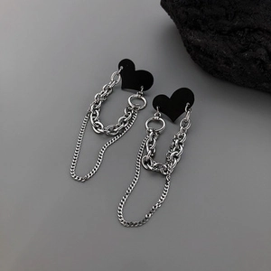 Detail view of punk style silver metal chains and matte black heart earrings on a rock base