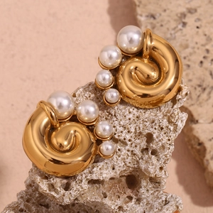 Macro detail of gold spiral earrings featuring elegant white pearls on a stone base