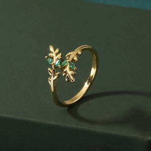Golden leaf ring with green marquise stones on a dark green matte surface
