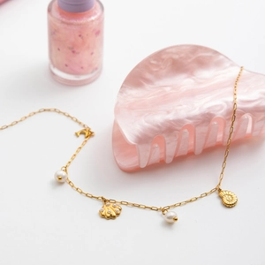 Detail of golden stainless steel necklace with delicate pearls and shell pendant accent